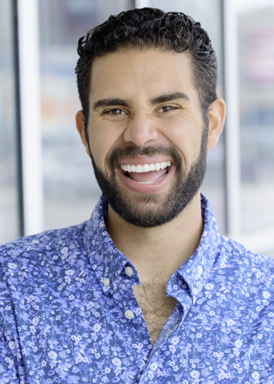 Nate is a light-skinned man with dark hair and a beard.  He is wearing a blue shirt with flowers on it. He is smiling.